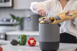 A person is sliding food scraps off a cutting board into a FoodCycler bucket.