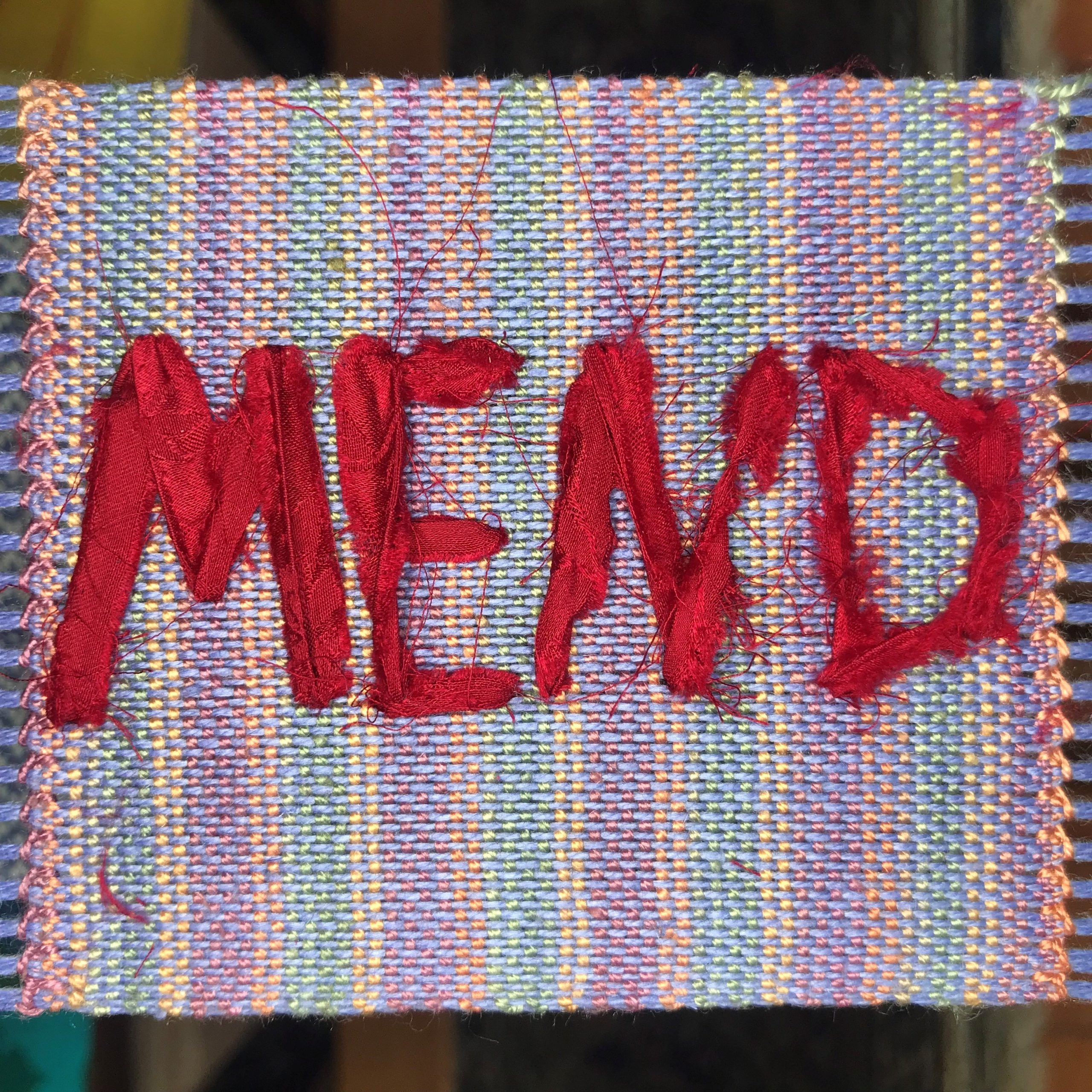 Fabric square with the word “MEND” hand‑stitched onto it.